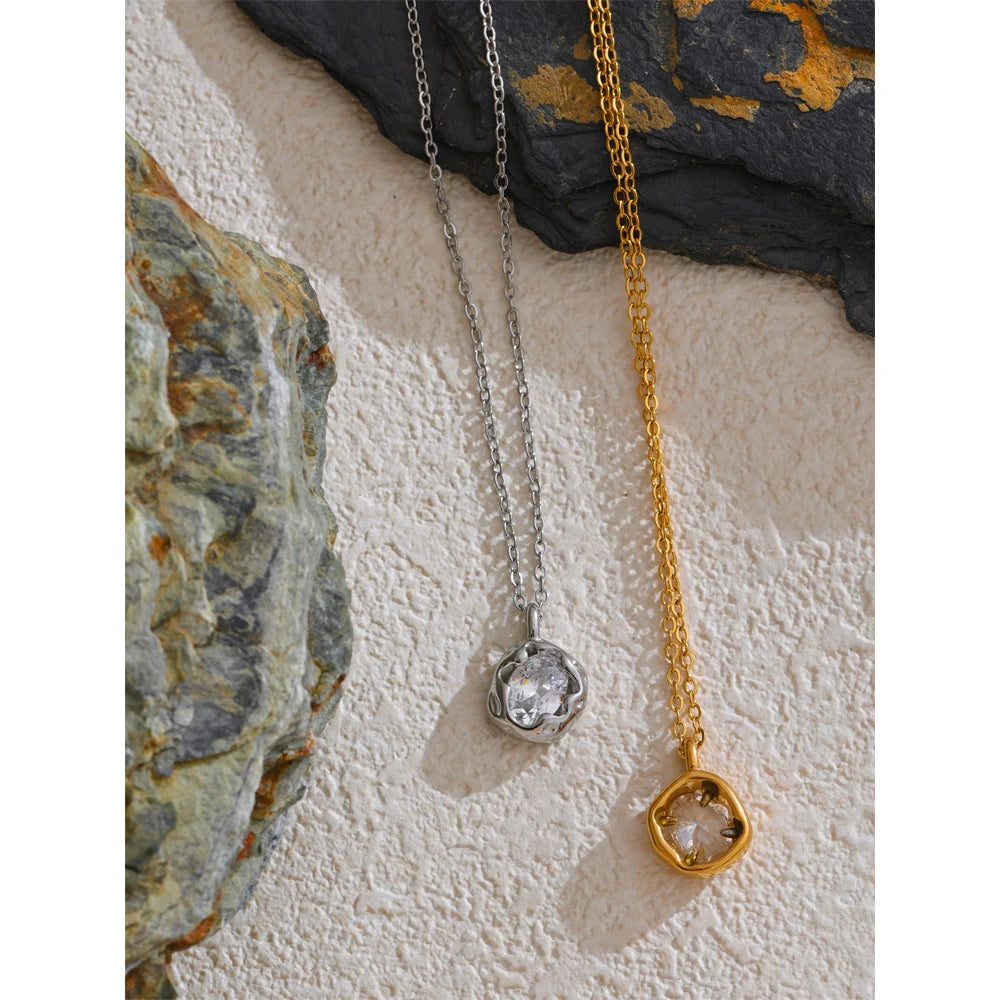 Colares feminino prata e dourado com pingente de cristal sobre superfície de pedra