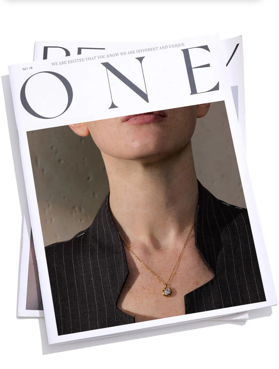 Colar dourado com pingente de pedra em revista, mulher com blazer risca de giz