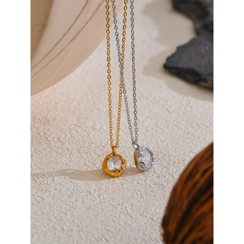 Dois colares com pingente redondo de cristal, um dourado e um prateado, sobre superfície clara.