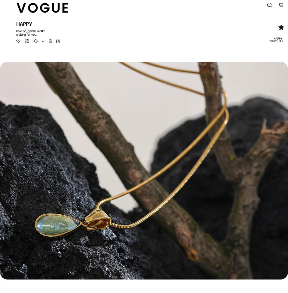 Colar dourado com pingente de pedra verde, exposto sobre galho e pedra preta, joias modernas.