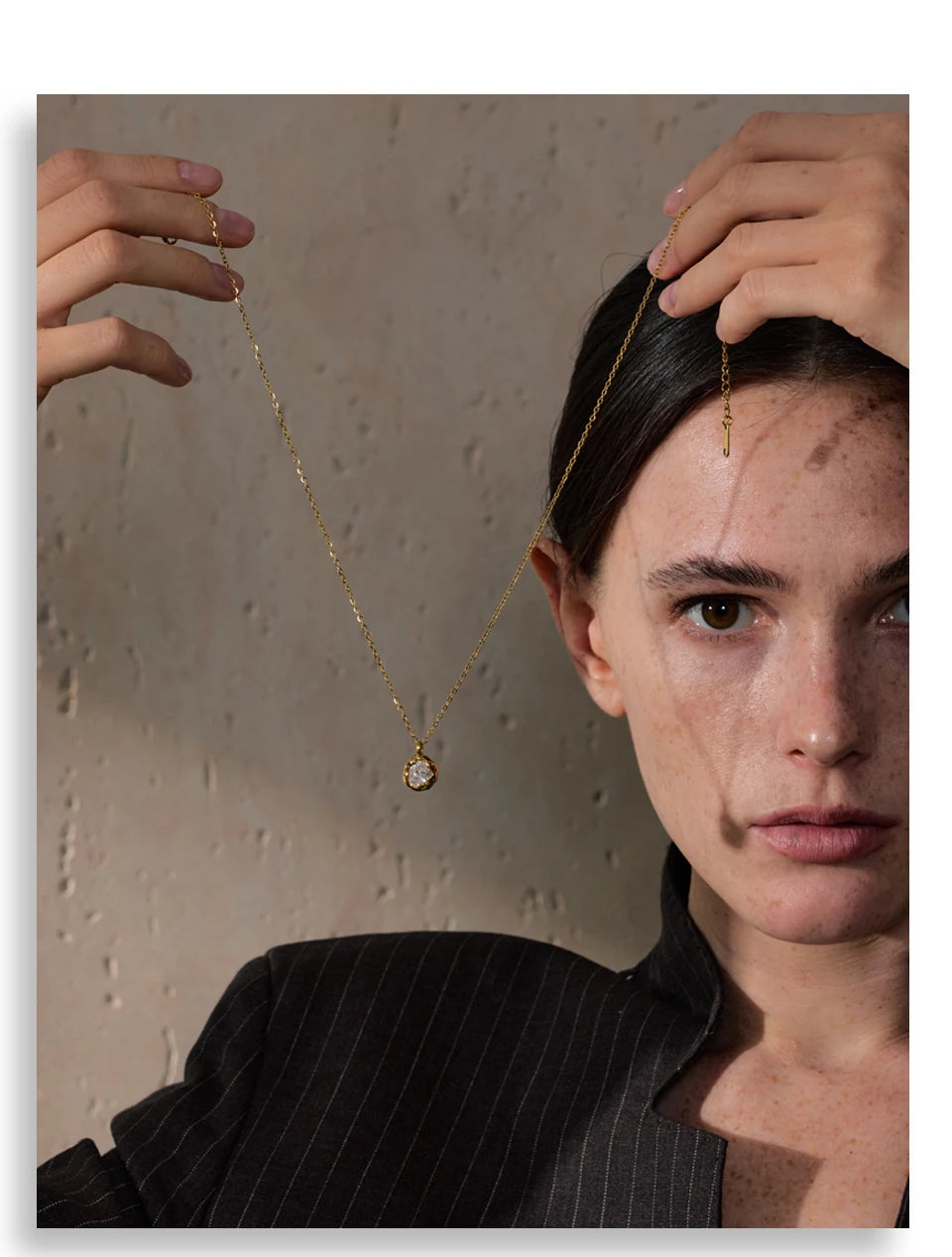 Mulher segurando colar dourado com pingente de pedra, fundo bege, moda elegante.